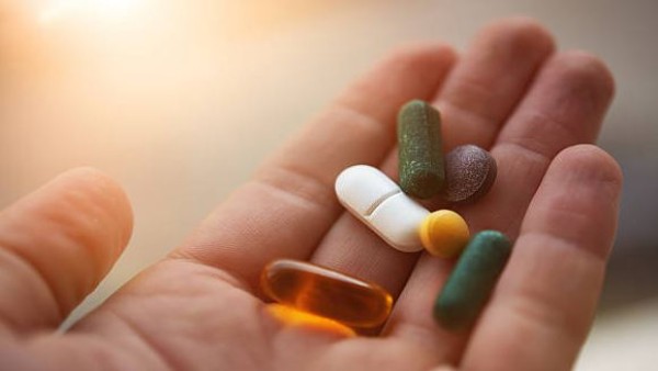 Tangan memegang beberapa tablet obat.