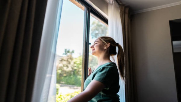 Seorang perempuan menikmati cahaya matahari pagi dari balik jendela, kebiasaan sederhana yang dikaitkan dengan kesehatan gula darah.