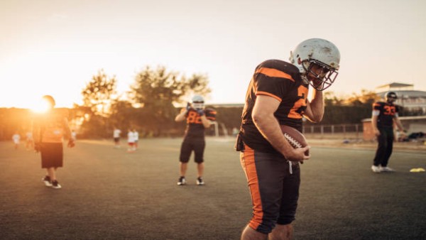 Ilustrasi pemain football memegang helm setelah mengalami benturan saat pertandingan.