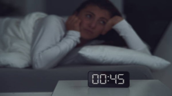Ilustrasi seseorang tidur tidak teratur di malam hari dengan suasana gelap dan jam digital menunjukkan waktu larut, menggambarkan gangguan pola tidur yang berkaitan dengan kesehatan jantung.