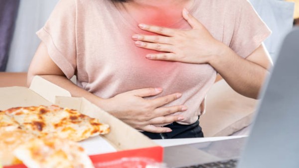 Ilustrasi seorang wanita mengalami sensasi panas di dada akibat asam lambung atau heartburn saat menikmati makanan.