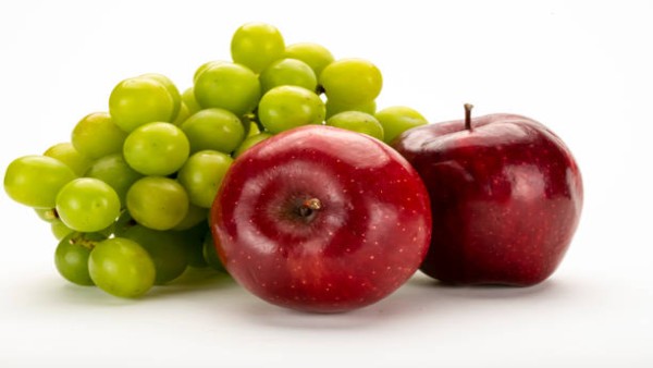 Perbandingan visual apel merah dan anggur segar di atas meja kayu dengan pencahayaan alami sebagai ilustrasi buah sehat untuk diet seimbang.