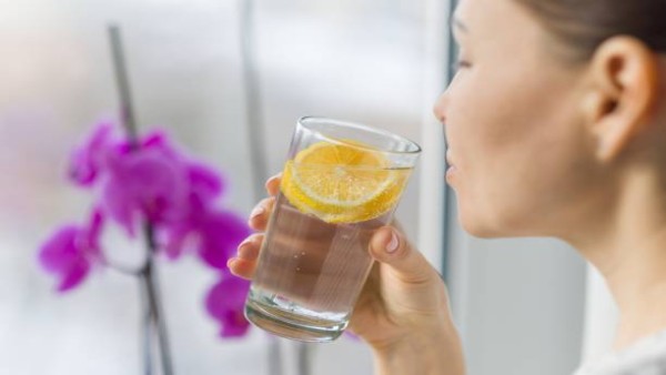 Seorang wanita dewasa menikmati segelas air lemon yang dipercaya memiliki berbagai manfaat untuk kesehatan dan kecantikan.