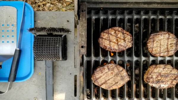 Ilustrasi burger panggang dan sikat pembersih grill berbahan kawat yang dapat menimbulkan risiko cedera jika serabut logamnya terlepas dan menempel pada makanan.